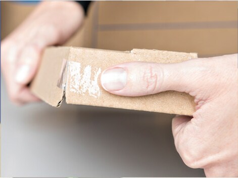Manos pegando una caja de cartón con Cinta Súper Adhesiva Scotch®.
